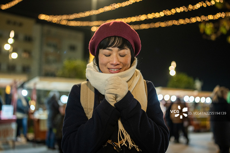 穿着冬装的快乐女子戴着围巾和贝雷帽，在夜市灯光下享受时光图片素材