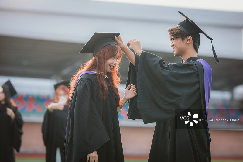毕业典礼前，一位快乐的亚裔男学生帮女同学调整学士帽图片素材