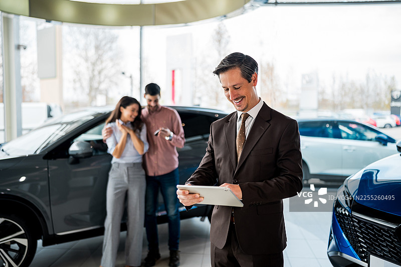 销售员使用平板电脑帮助一对快乐的夫妇购车图片素材