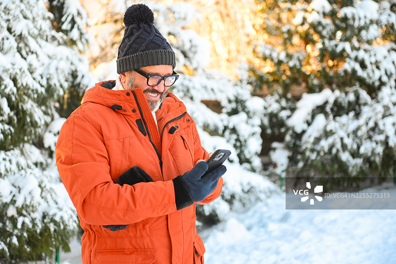 身着冬装的成熟男士在冬季的自然环境中玩手机图片素材