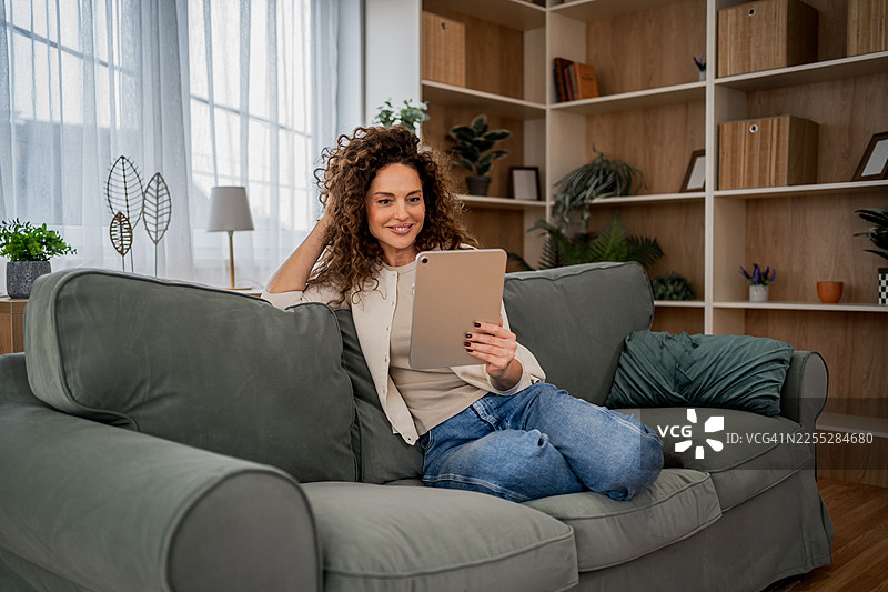 女子在家中舒适地躺在沙发上使用平板电脑图片素材