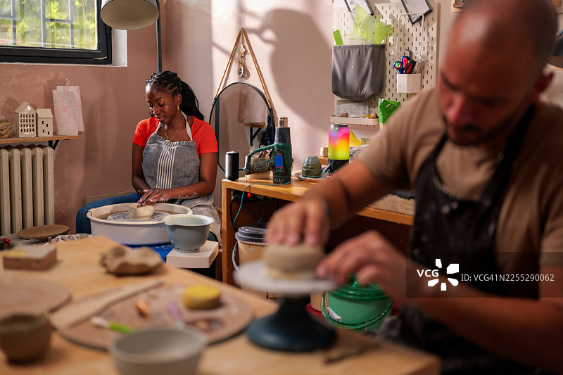 在陶艺工作室里，两位工匠——一位年轻女子和一位中年男子——正在用双手和工具塑造和制作陶瓷器皿。图片素材