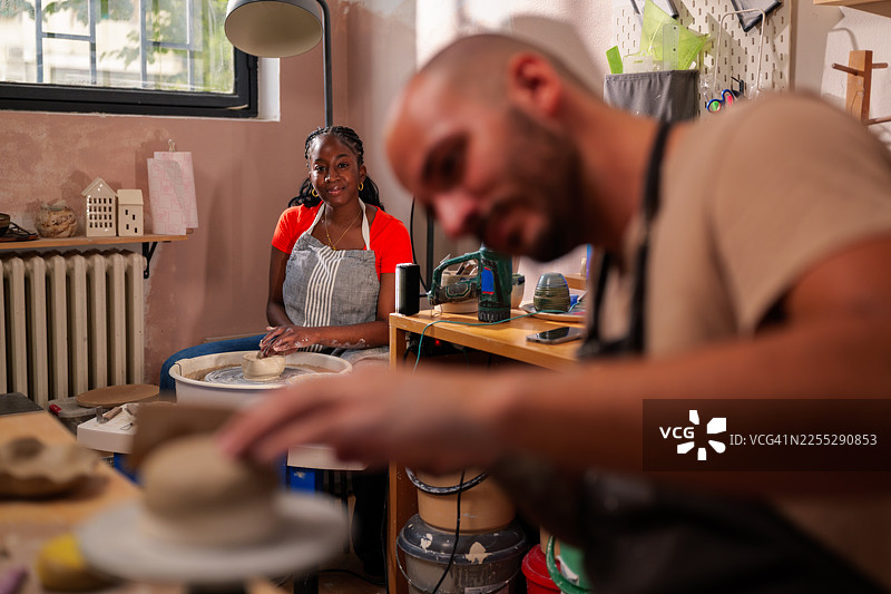 两位工匠正在陶艺工作室用粘土工作，使用陶轮和其他工具塑造和制作各种陶瓷器皿。图片素材