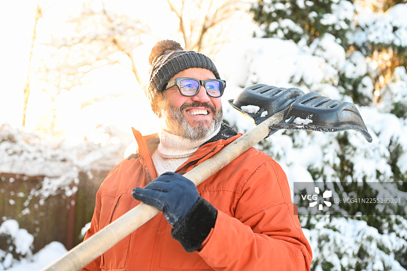 一位成熟的成年男子正在花园里铲雪图片素材