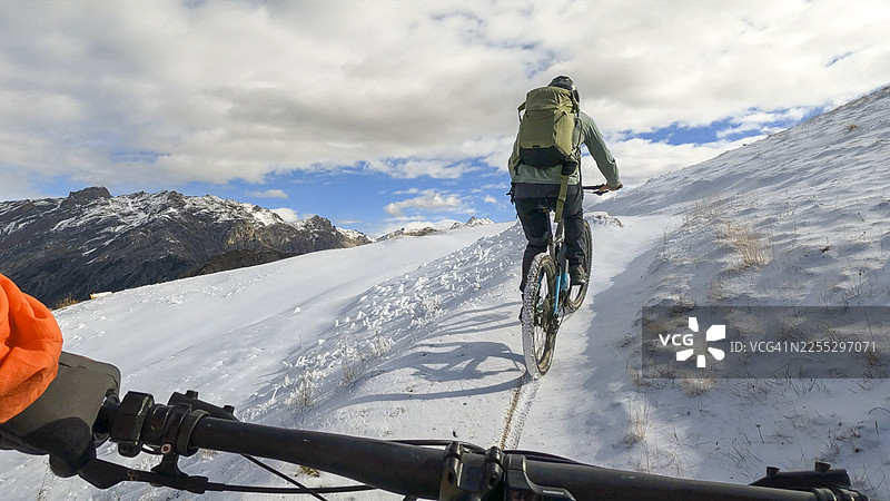 第一人称视角，跟随一名年轻男子骑着电动山地自行车在雪地小径上行驶图片素材