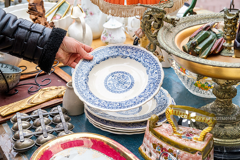 女子在户外集市摊位上查看白色瓷盘，展示着手工制作的复古陶瓷收藏品图片素材