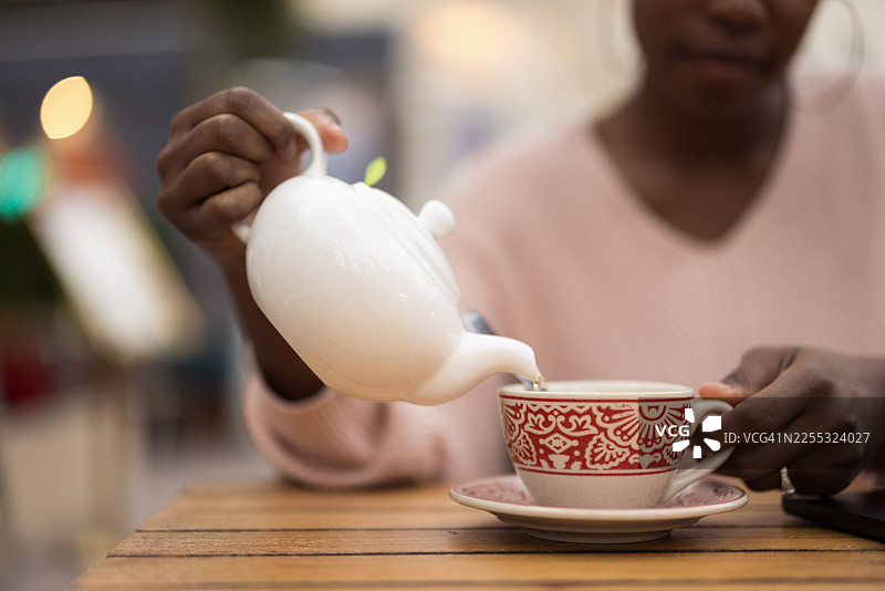 一位女士正从白色茶壶中向红白相间的茶杯里倒茶图片素材
