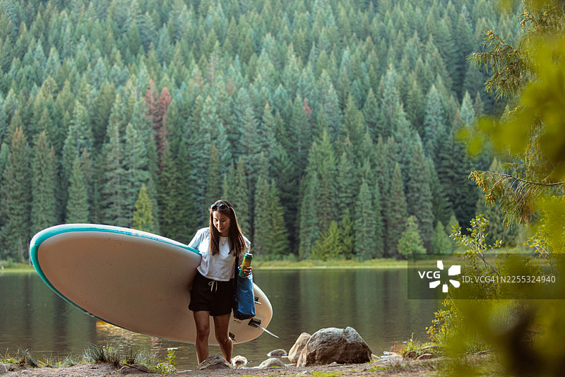 女子扛着桨板在山间湖泊旁图片素材