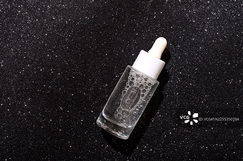 一个装有透明精华液的玻璃滴管瓶，背景为黑色。非常适合美容、护肤和健康宣传活动，突出保湿、纯净和专业化妆品图片素材
