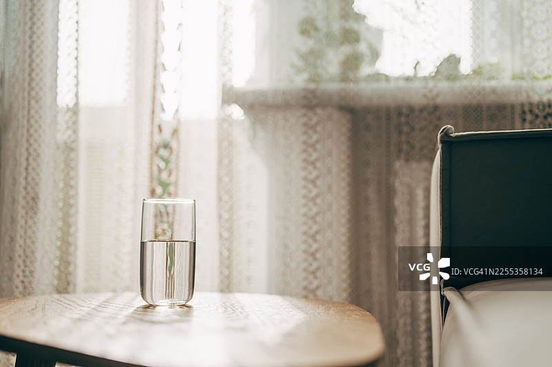 一个装有干净清澈的水的玻璃杯，投下锐利的阴影，放在一张白桌子上图片素材