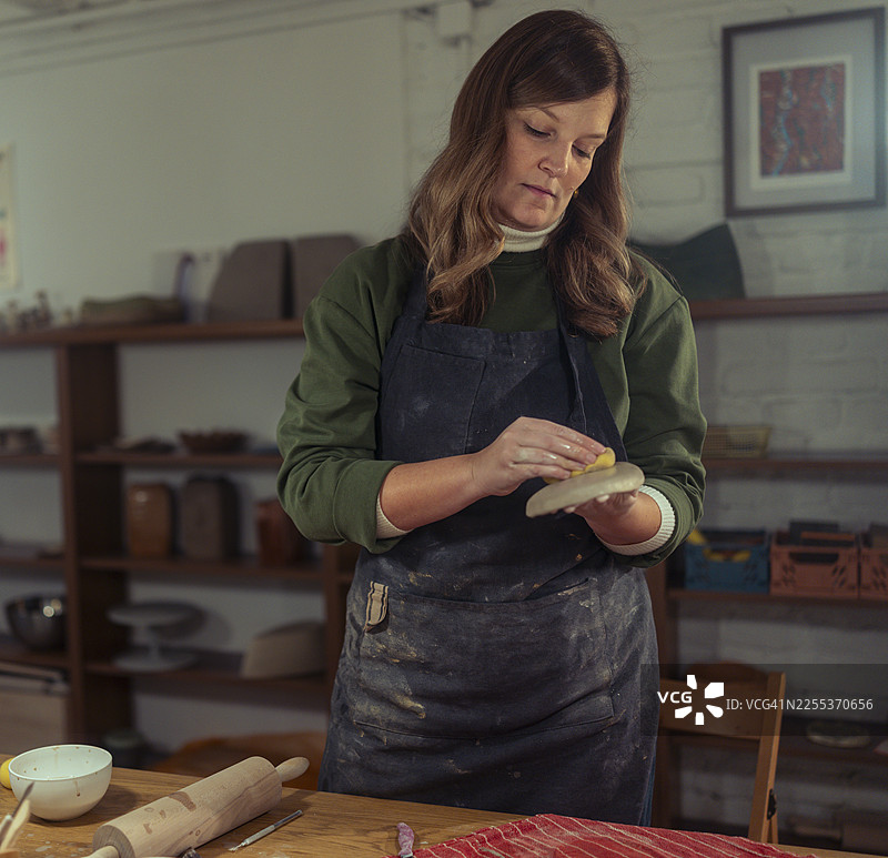 一位穿着围裙的专注女性正用黄色海绵打磨湿陶土的正面照图片素材