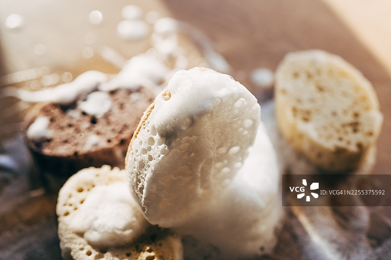 带有泡沫的天然洗碗海绵，背景为米色。环保家务用品。图片素材