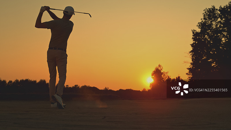 高尔夫球手在日落时分练习沙坑击球图片素材