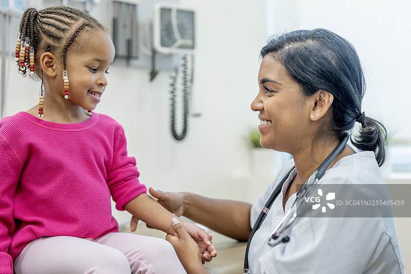 南亚护士在诊所检查小女孩的手臂，友好的儿科健康访问图片素材