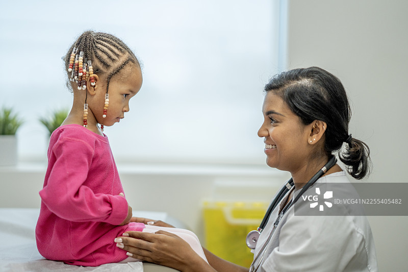 南亚女医生在儿科检查时与非裔美国小女孩互动图片素材