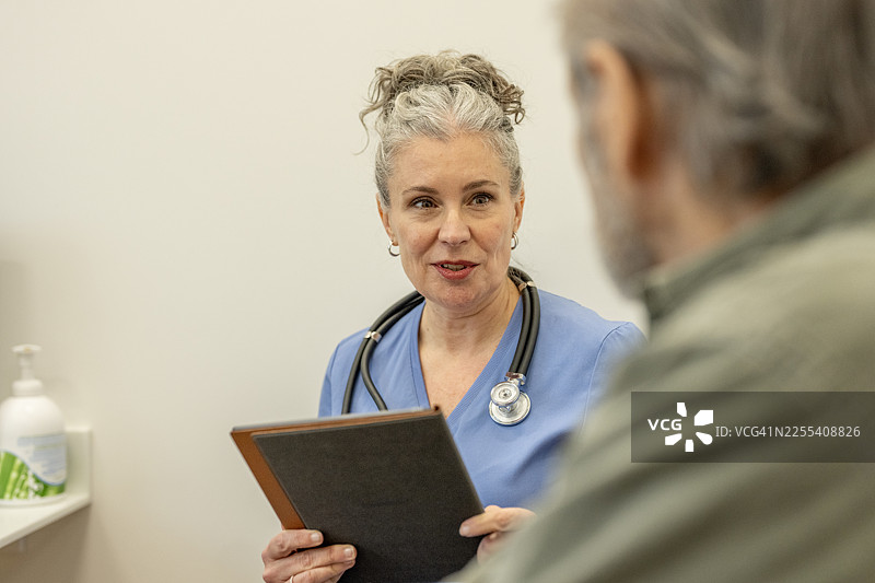 今日就诊时，经验丰富的女护士在诊所内，手持病历夹和听诊器，与患者讨论护理事宜。图片素材