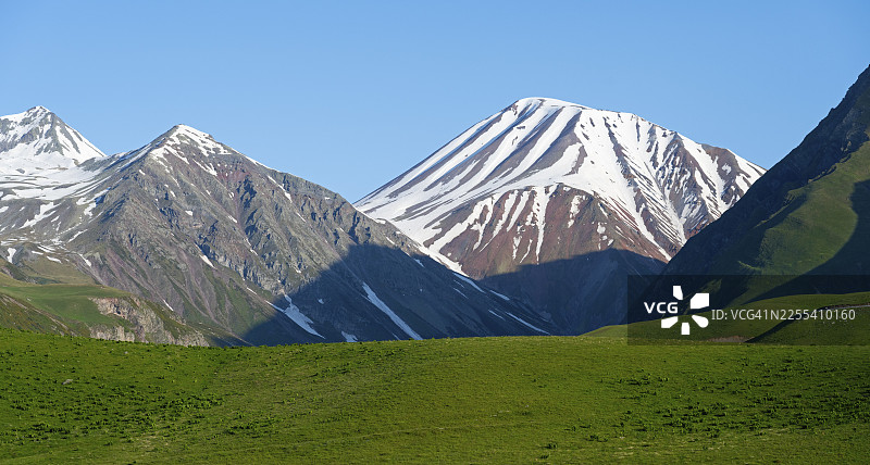 雄伟的雪山，前景是绿色的田野，位于格鲁吉亚姆斯赫塔-姆季阿涅季地区格鲁吉亚军事大道克韦谢蒂和古达乌里之间的景观，高加索山脉图片素材