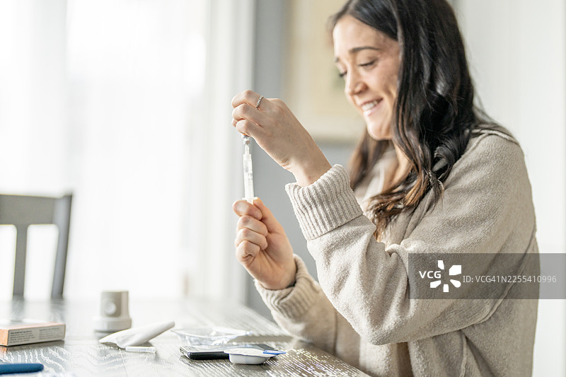 在家精心准备医疗注射器的女性，用于个人护理图片素材