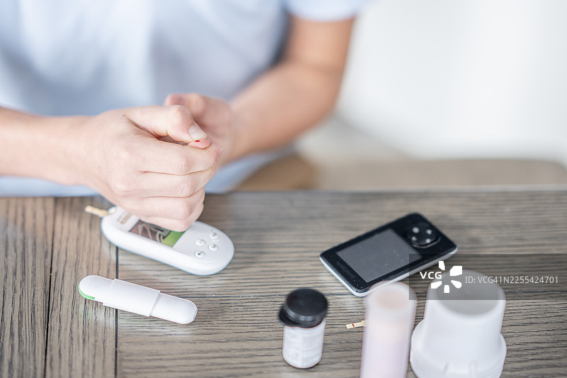 亚洲女性在桌上用血糖仪、胰岛素瓶和医疗器械检测血糖图片素材