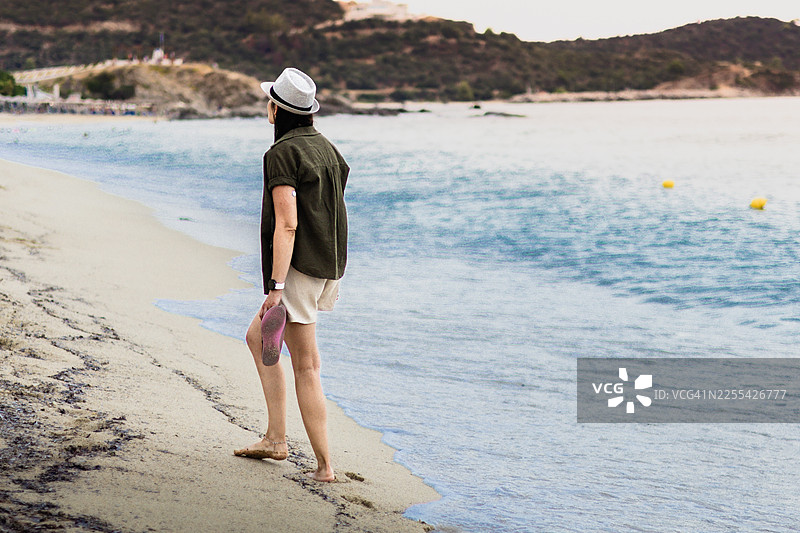 戴着草帽的女人在海边。手臂上的连续血糖监测仪、智能手表、手机和防水 CGM 保护套让糖尿病患者的旅行和生活更轻松。图片素材