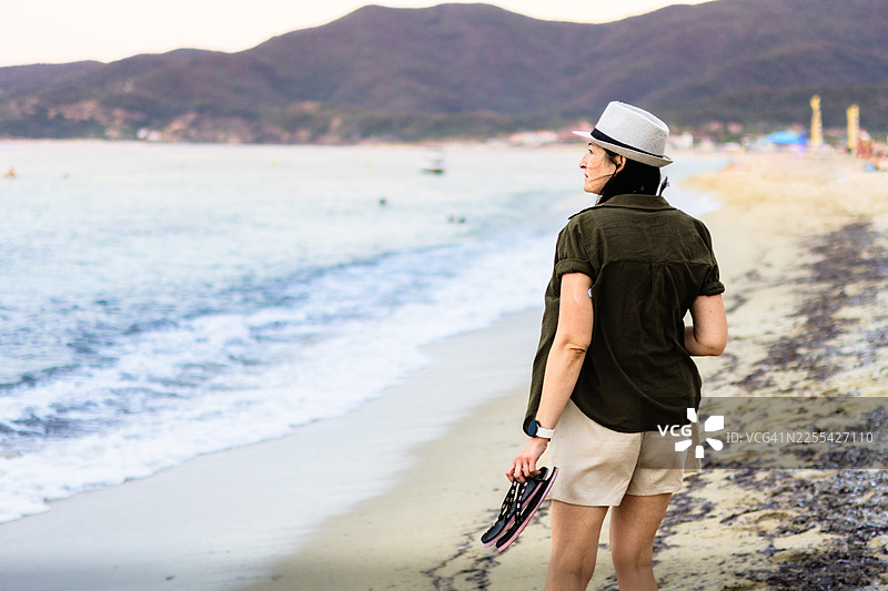 戴着草帽的女人在海边。有了手臂上的连续血糖监测仪、智能手表、手机和防水CGM保护装置，糖尿病患者的旅行和生活会更轻松。图片素材