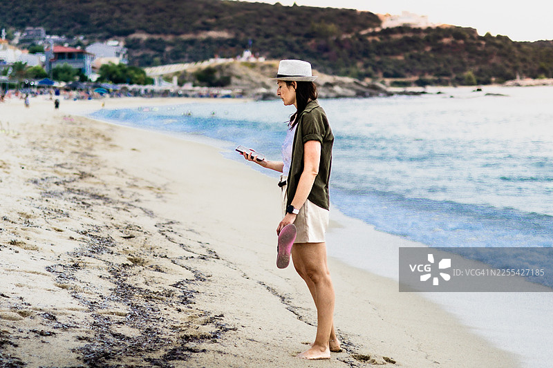 戴着草帽的女子在海边，手臂上戴着持续葡萄糖监测仪（CGM）、智能手表、手机，并配有防水CGM保护套，使糖尿病患者的旅行和生活更加轻松。图片素材
