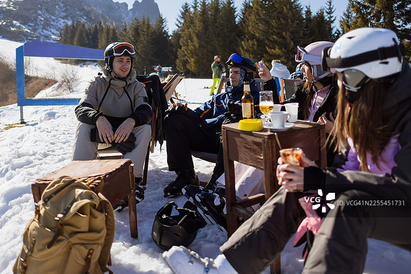 在阳光明媚的滑雪度假村露台上，朋友们一边喝着饮料一边聊天图片素材