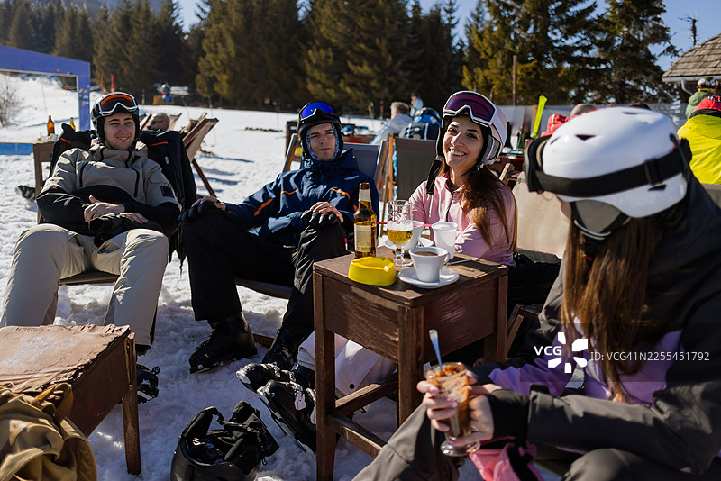 一群朋友在阳光明媚的滑雪度假村咖啡馆里，一边饮酒一边交谈，享受着欢乐时光。图片素材