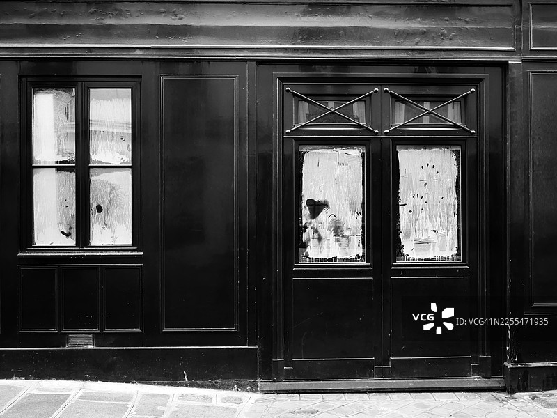 法国巴黎一家废弃酒吧的黑色外墙，带有门窗（玻璃漆成白色）。铺砌的人行道。图片素材