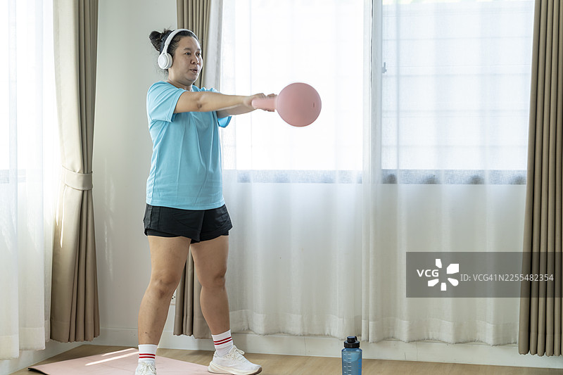 年轻女子在家使用壶铃锻炼，追求力量和健康的生活方式图片素材