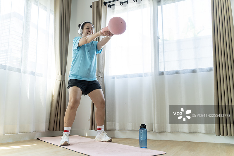 年轻女子在家中使用壶铃锻炼，以增强力量和健康生活方式图片素材
