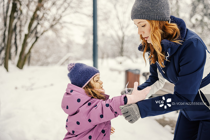 冬天雪地里，母亲帮女儿戴上手套图片素材