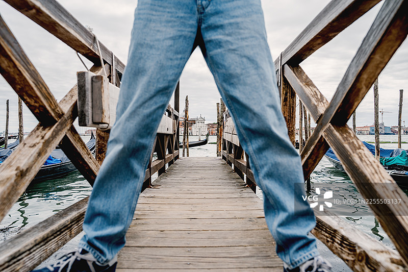 意大利威尼斯穆拉诺岛和布拉诺岛景观，透过男孩的腿可以看到木制码头和贡多拉，里瓦德利斯基亚沃尼图片素材