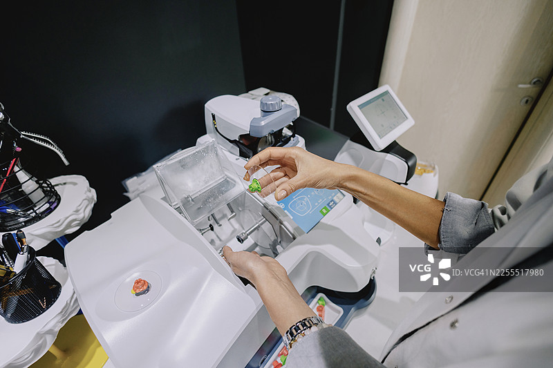 在光学实验室里，一位女性眼科医生或验光师正在操作一台切割或打磨镜片的机器。图片素材