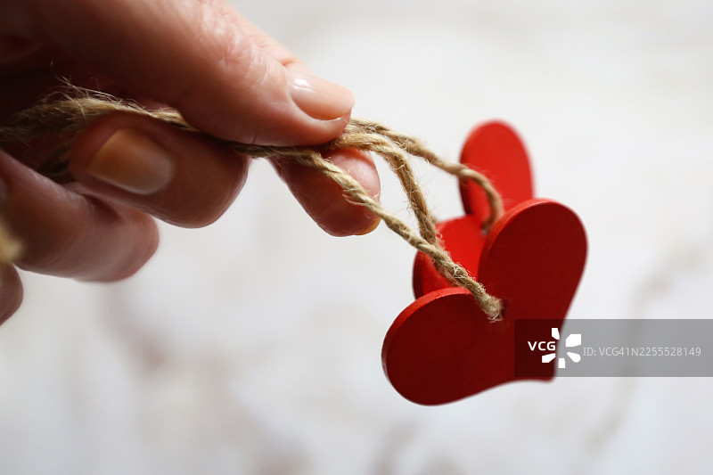 女性的手握着两个红色的木制心形纪念品，象征着爱与信任图片素材