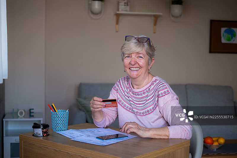 一位年长的女性微笑着展示卡片进行在线支付图片素材