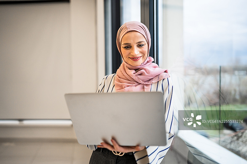 戴着头巾的穆斯林女商人在使用笔记本电脑时面带微笑图片素材