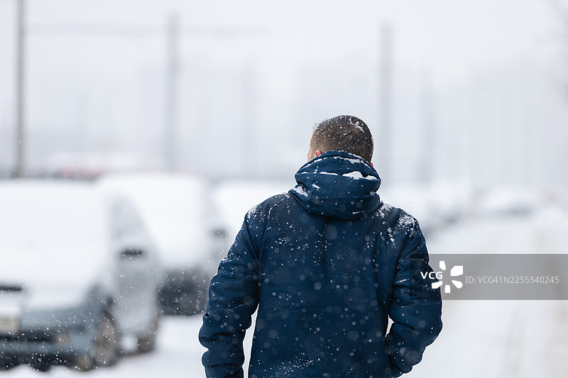 寒冷冬日，一名男子走在雪中的城市街道上图片素材
