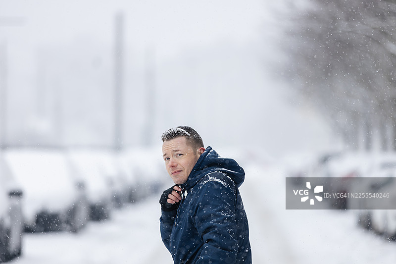 寒冷冬日，男人走在白雪覆盖的城市街道上图片素材