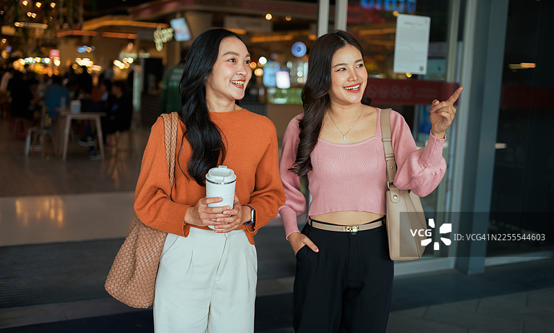 两位年轻的女性朋友面带笑容，在明亮的购物中心边走边聊，享受着闲暇时光图片素材