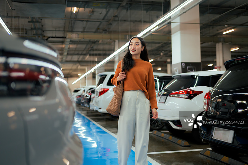 年轻的亚洲女性正在地下停车场寻找她的汽车，她挎着一个休闲包图片素材