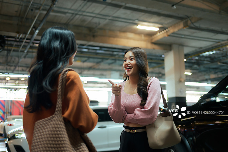 两位开朗的年轻女性在地下停车场进行热烈交谈并互相指点图片素材