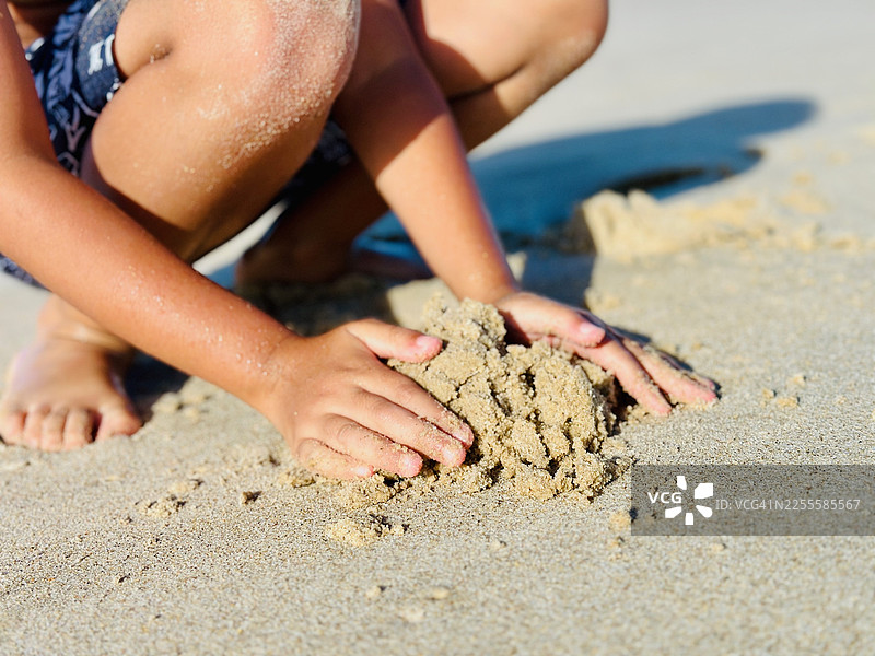 特写：孩子在海滩上用手堆沙堡图片素材