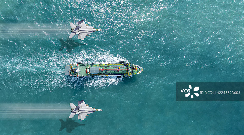 空中俯瞰，战斗机在海上飞越油轮。这一概念说明了保护油轮免受空中和海上侵略者的侵害。图片素材