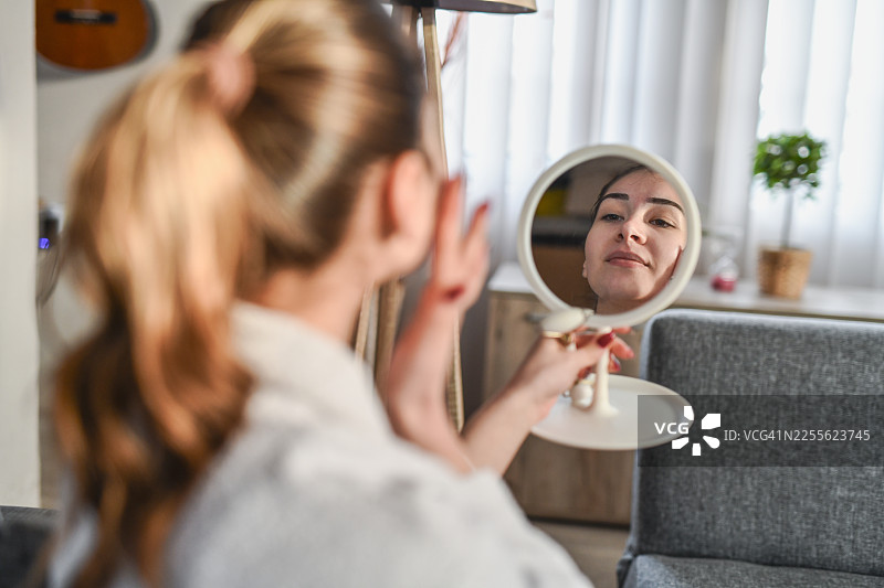 居家水疗日：女子在圆形镜子中映照出使用玉石滚轮的画面图片素材