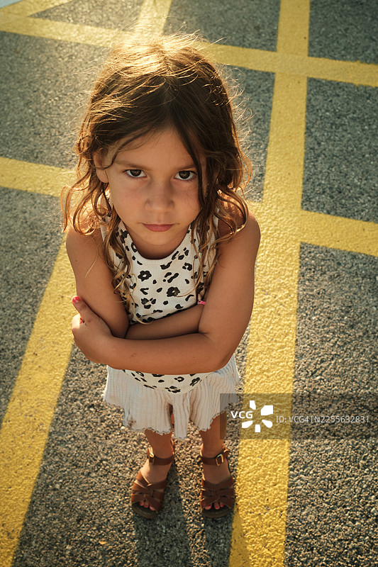 小女孩双手抱臂，撅着嘴，站在黄线上图片素材