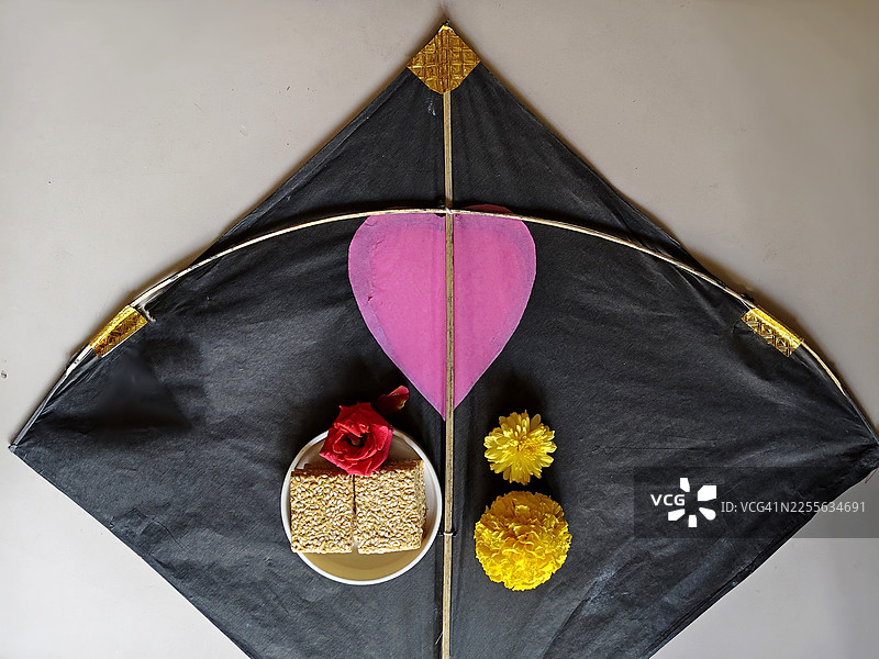 这张图片捕捉了充满活力的冬季丰收节——马卡尔·桑克拉蒂/北方节的精髓，画面中有放飞的风筝、芝麻糖/gajak、til Chikki、印度脆饼、万寿菊和玫瑰花，背景为白色。图片素材