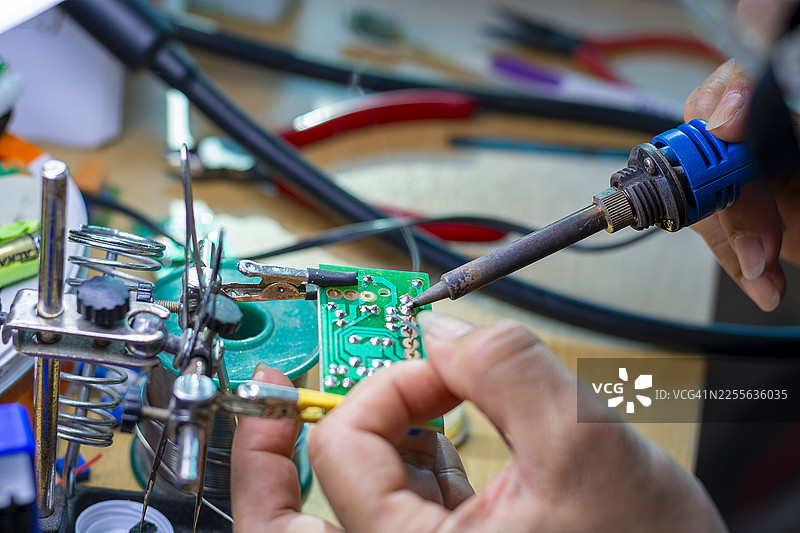 戴着蓝色手套的手在印刷电路板的生产背景下，拿着一块PCB芯片组件图片素材