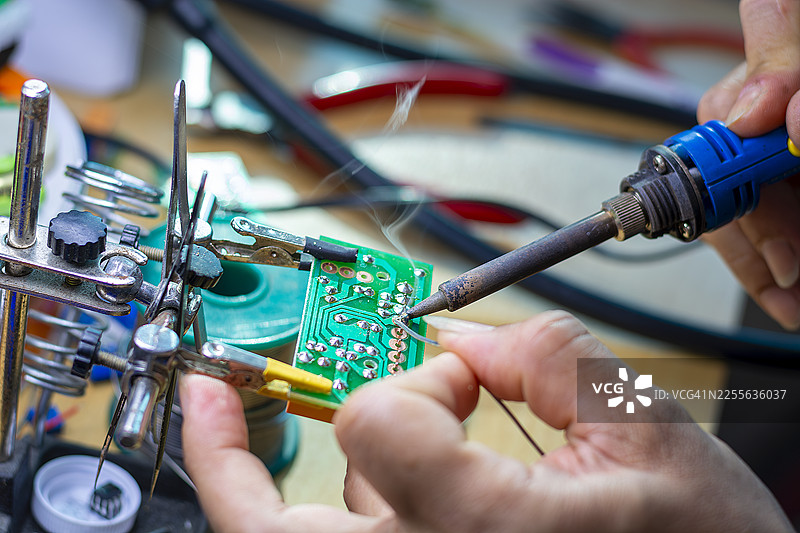 戴着蓝色手套的手在印刷电路板生产背景上拿着一块PCB芯片组件图片素材