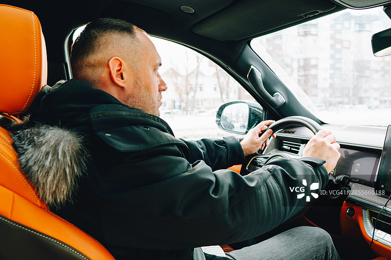 冬季通勤时，一名男子在车内驾驶，车辆内饰为橙色图片素材